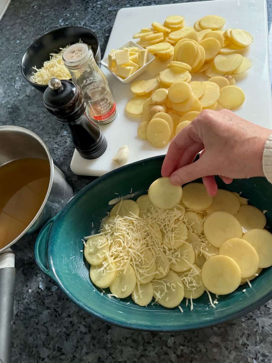 Layering thin potato slices with cheese in a buttered ovenproof dish