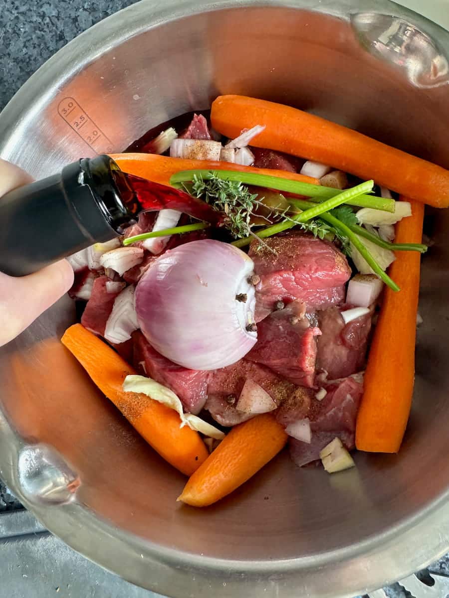 Pouring red wine into a marinade for classic Boeuf Bourguignon.