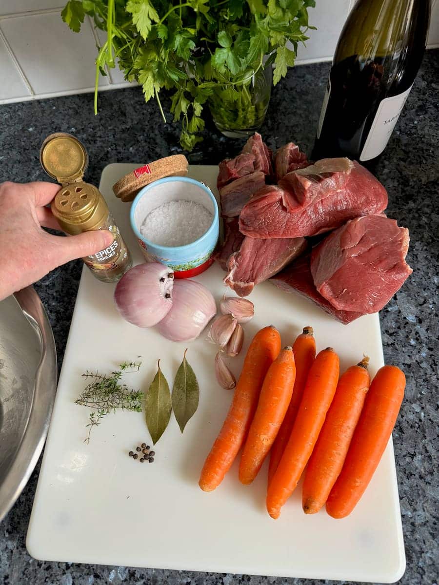 Ingredients for the marinade of Boeuf Bourguignon: chuck steak, onion, spices, red wine, and carrots.
