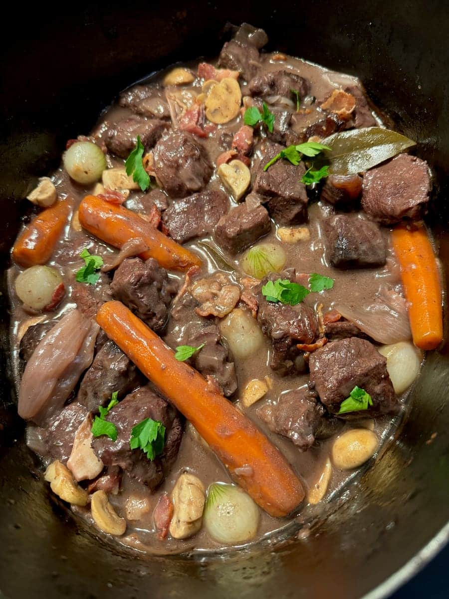 Crock pot of Boeuf Bourguignon with carrots, mushrooms, and pearl onions topped with parsley.