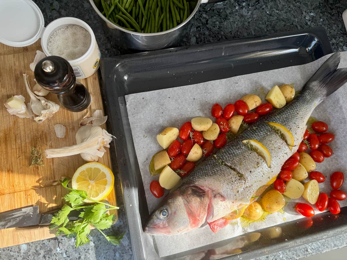 Whole sea bass laid in a baking dish with herbs and vegetables