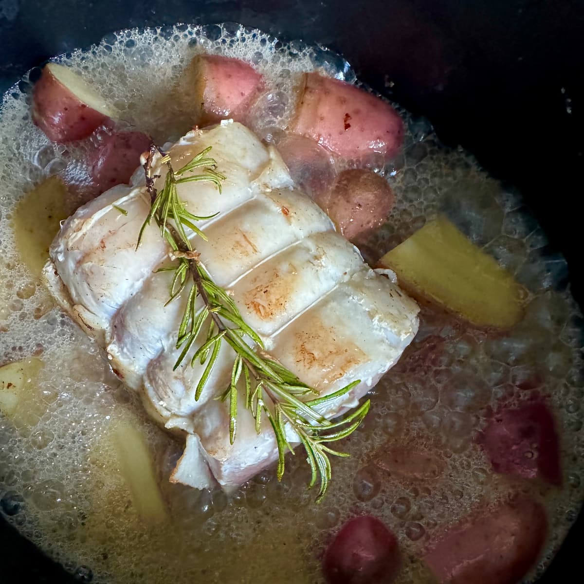 Tender pork roast with apple cider, surrounded by potatoes and rosemary.
