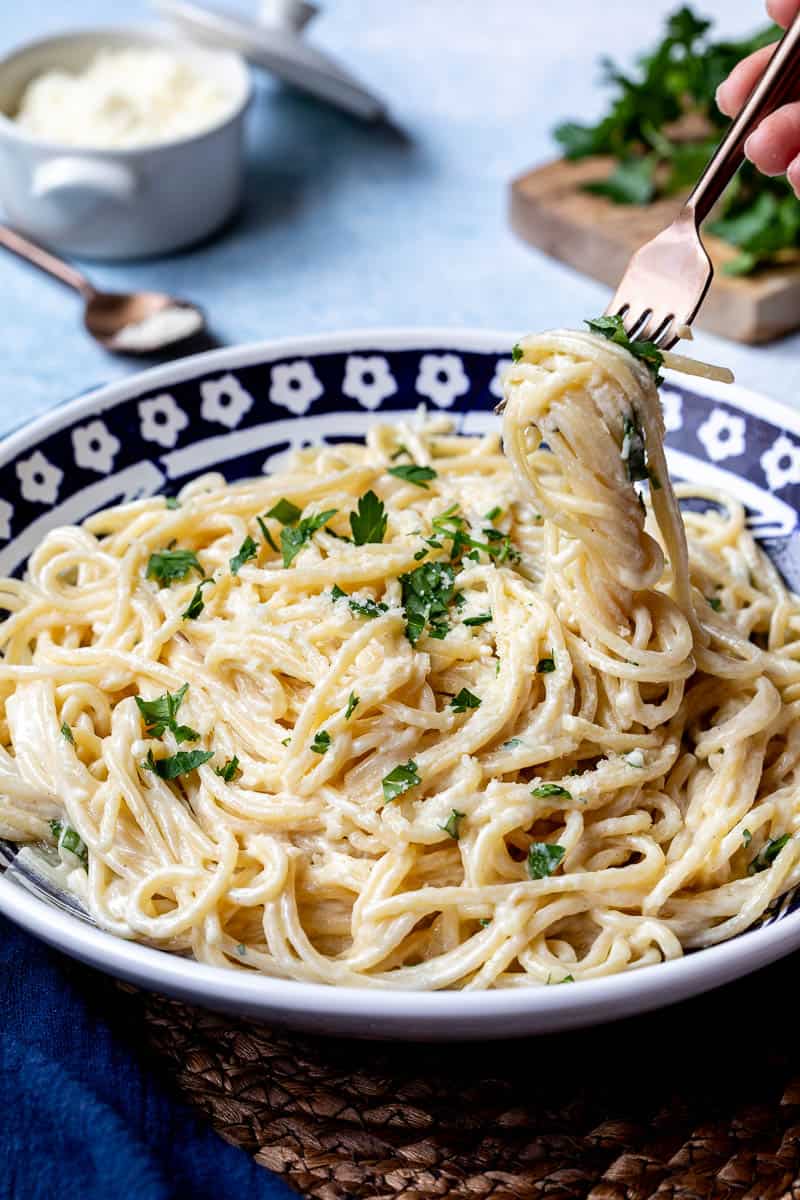 A bowl of spaghetti Alfredo with strands of pasta being lifted by a fork