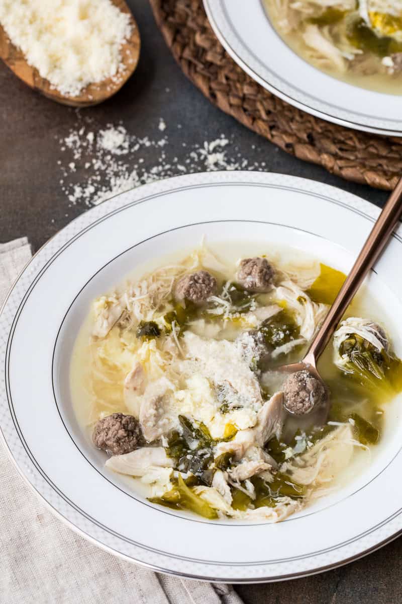 bowl of Italian Wedding Soup with spoon in front of parmesan cheese
