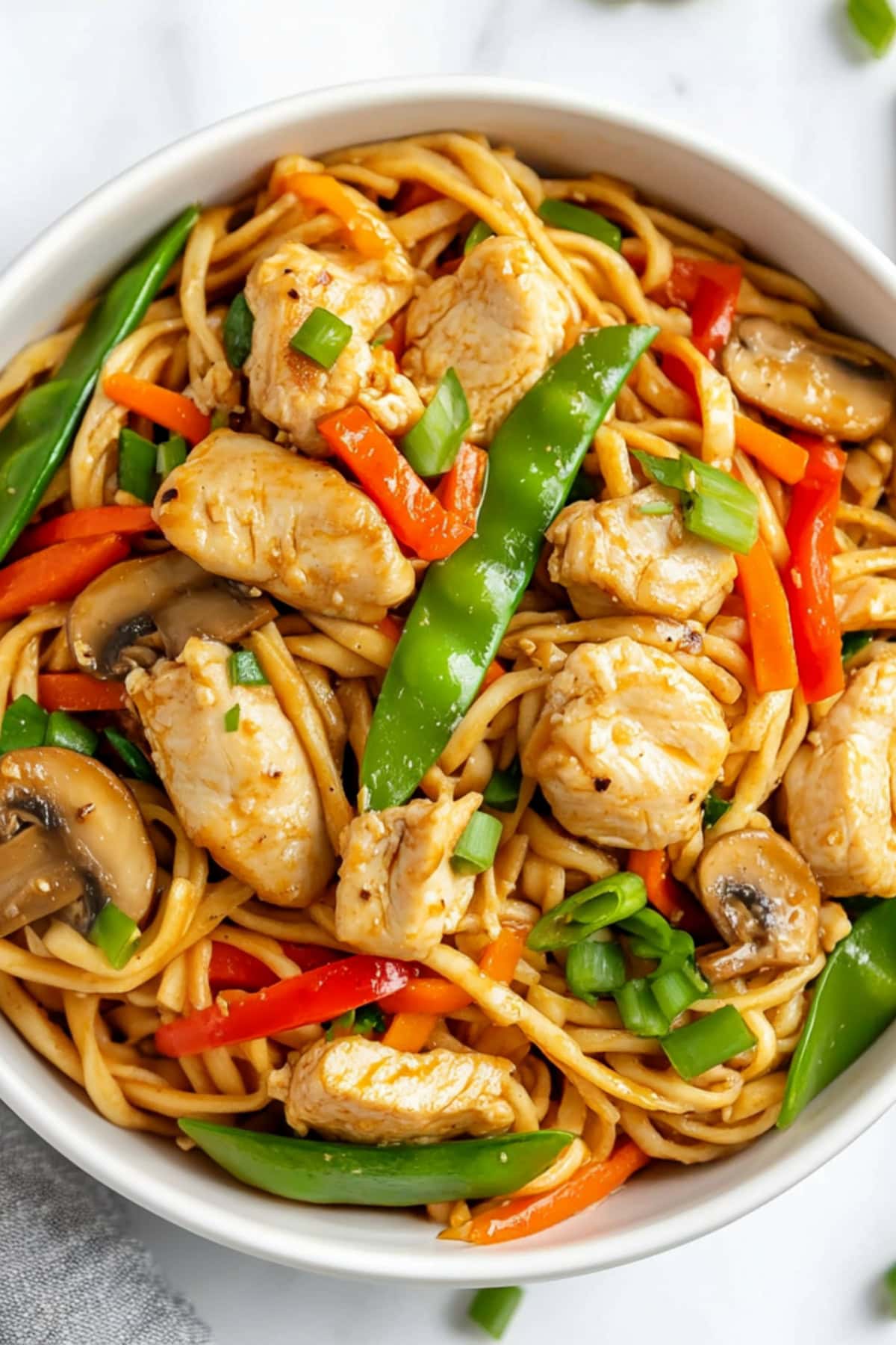 A plate of chicken lo mein noodles stir-fried with colorful vegetables, including bell peppers, carrots, and snow peas.