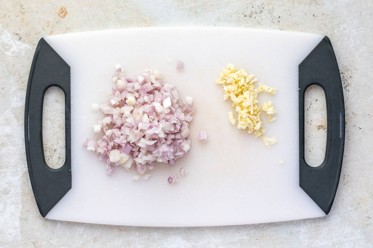 Chopped shallots and garlic on a cutting board.