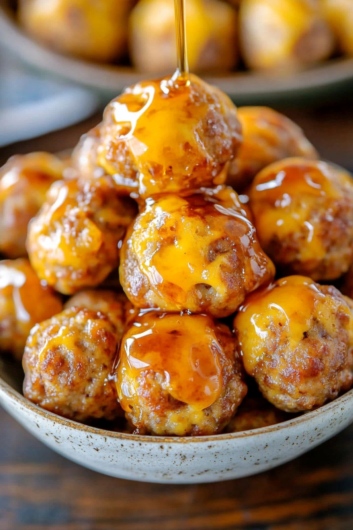 Honey dripping over bunch of sausage pancakes in a white bowl.