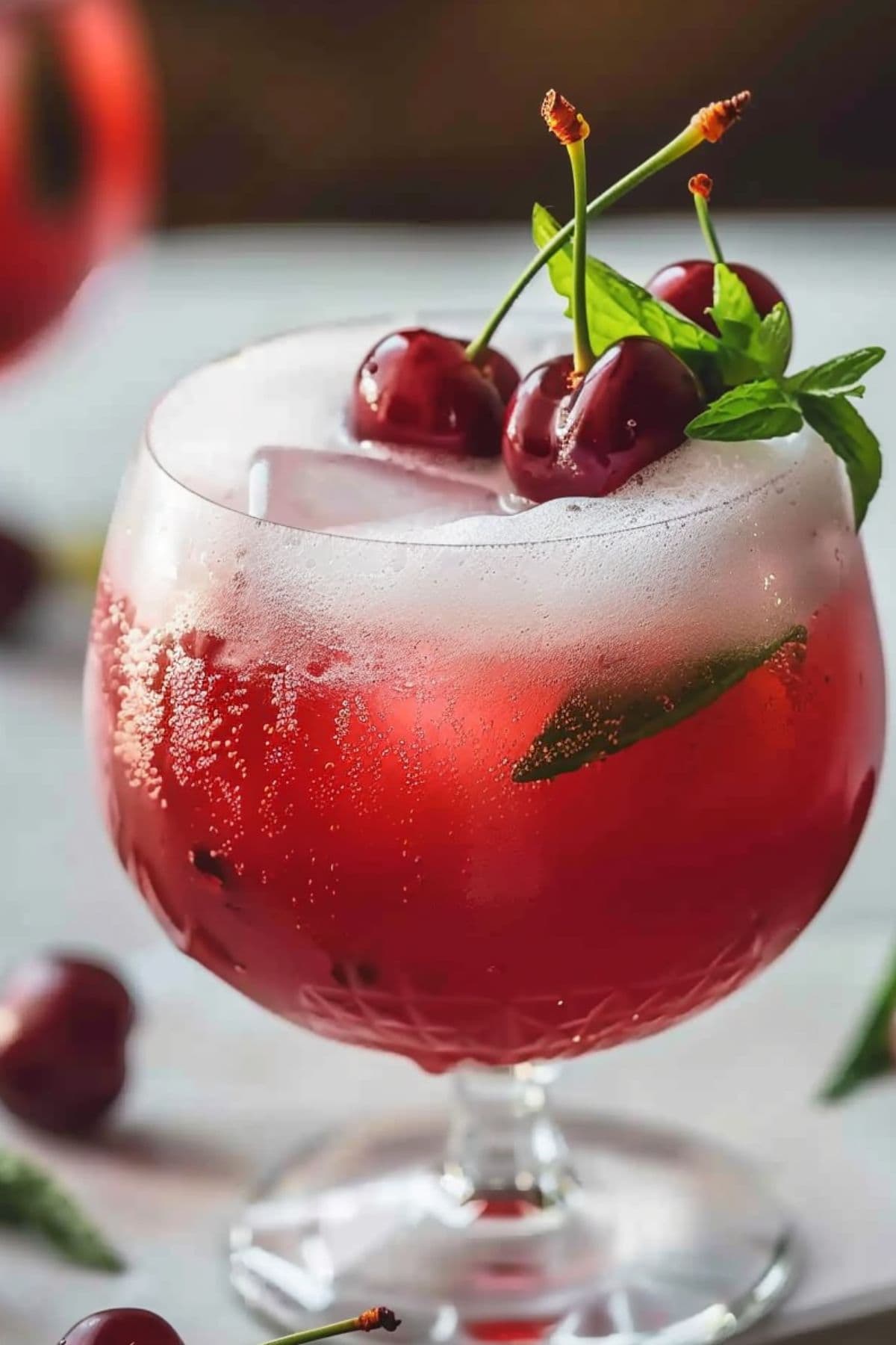 A serving of refreshing cherry vanilla fizz in a cocktail glass garnished with cherries and lemon mint sprigs.