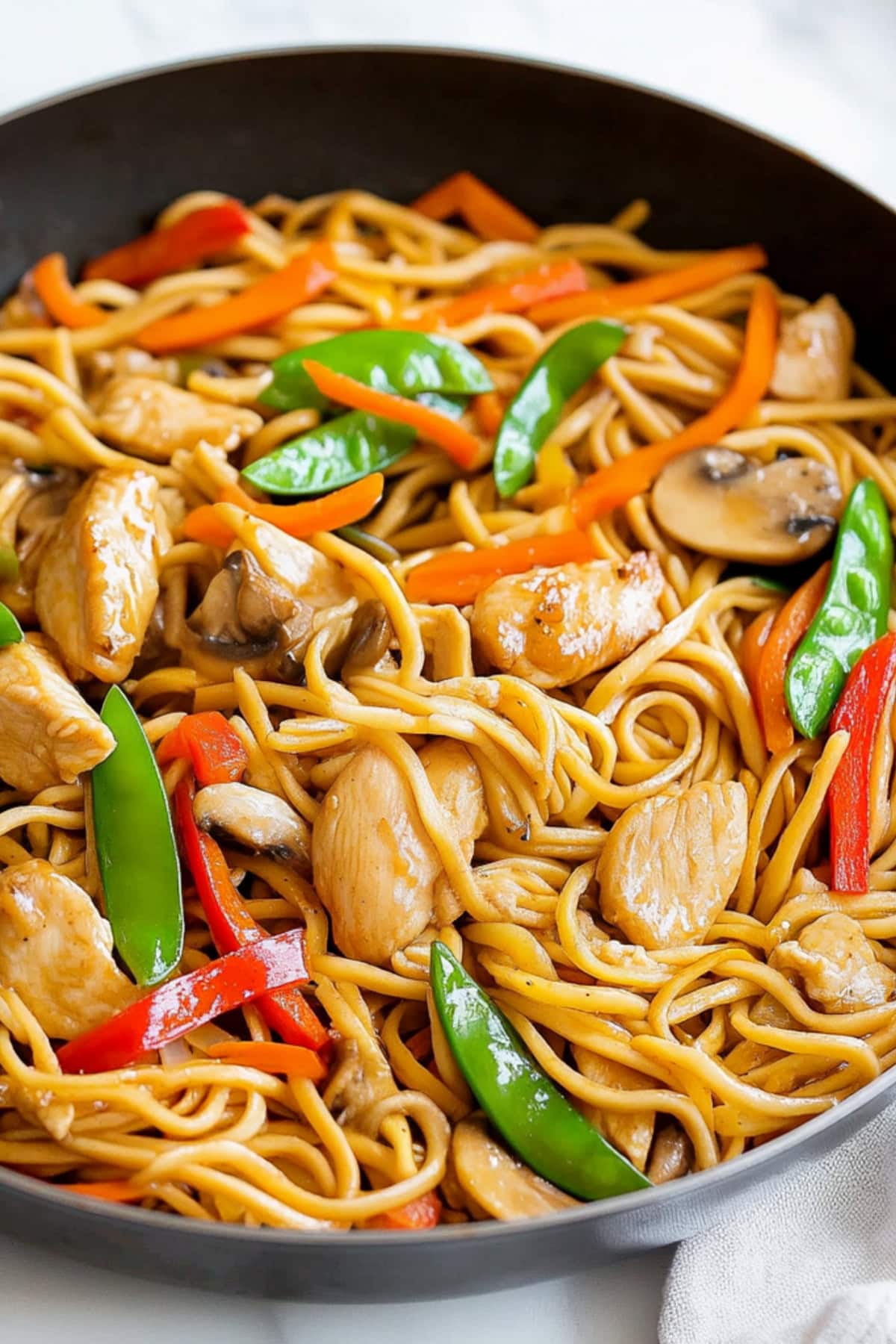 Chicken lo mein with snow peas, bell peppers, and carrots in a skillet.