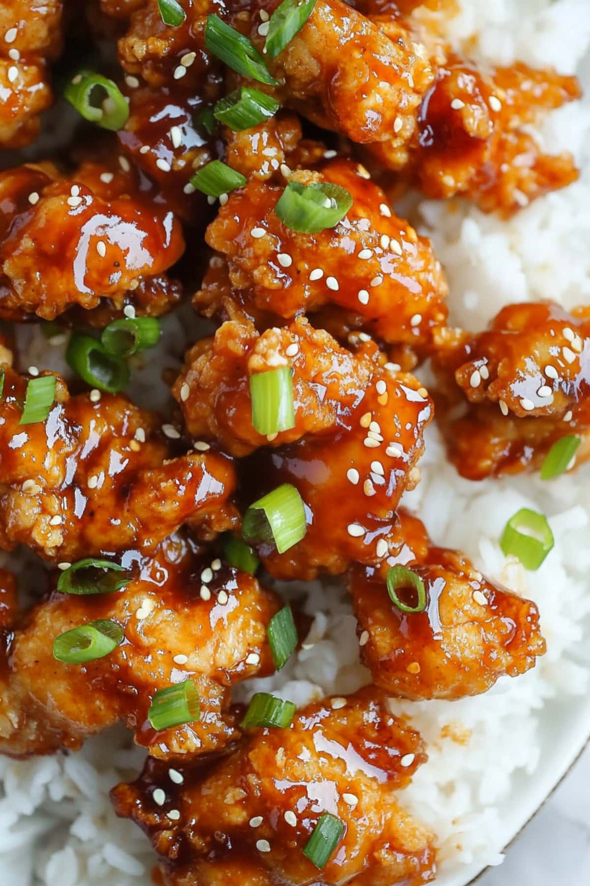 A close-up of sesame chicken with chopped onions, accompanied by rice.