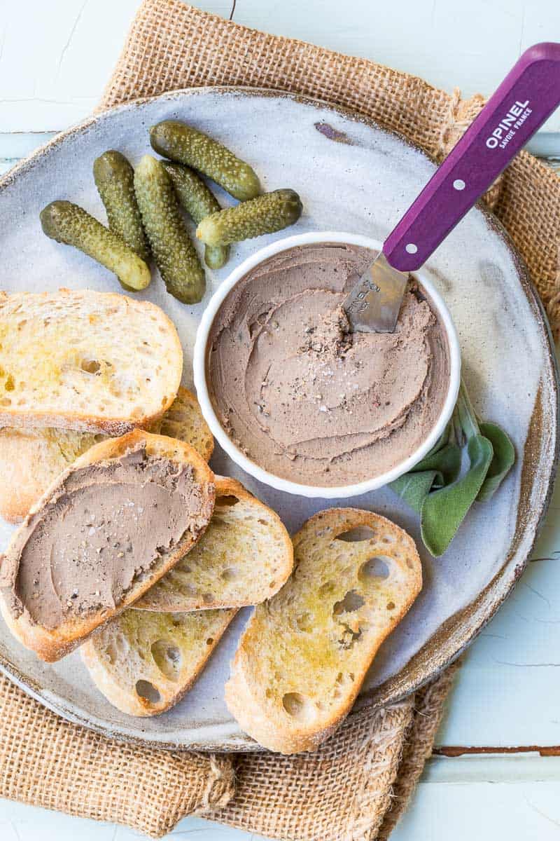 Chicken liver pâté on plate with baguette toasts and cornichons.