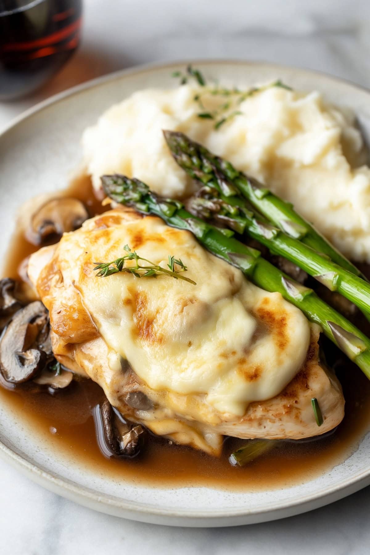 Chicken madeira served on a plate with mushrooms and asparagus.