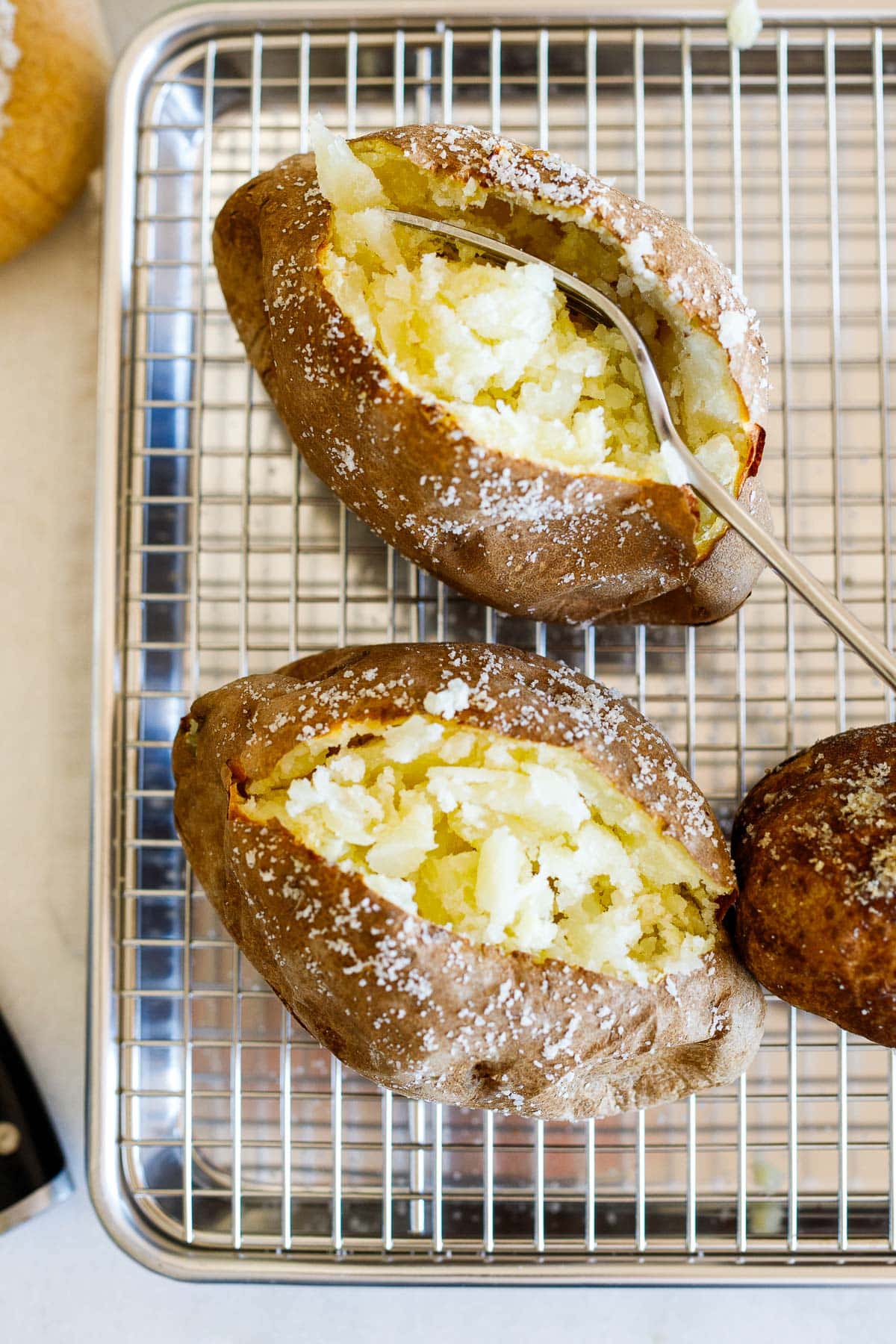 A perfectly baked potato cut open to reveal its fluffy interior with a fork placed inside.