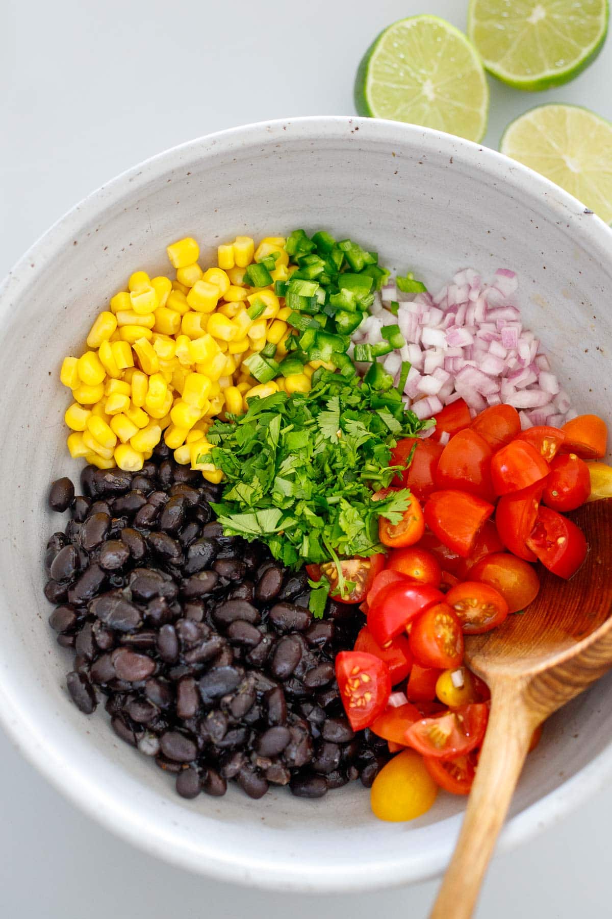 Mixing bowl filled with black beans, corn, jalapeño, onion, and tomatoes before mixing.