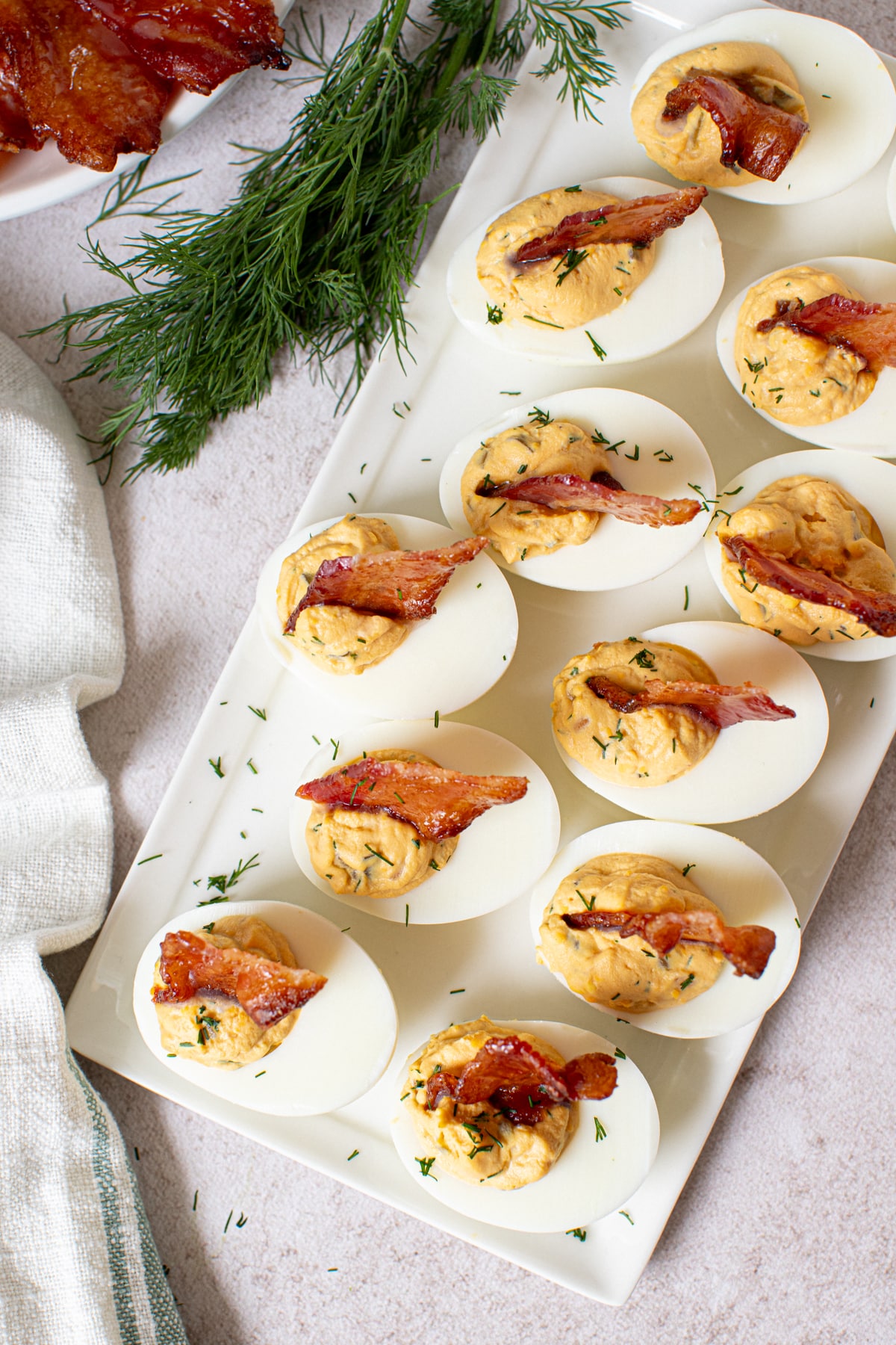A dozen deviled eggs with candied bacon on a white platter.