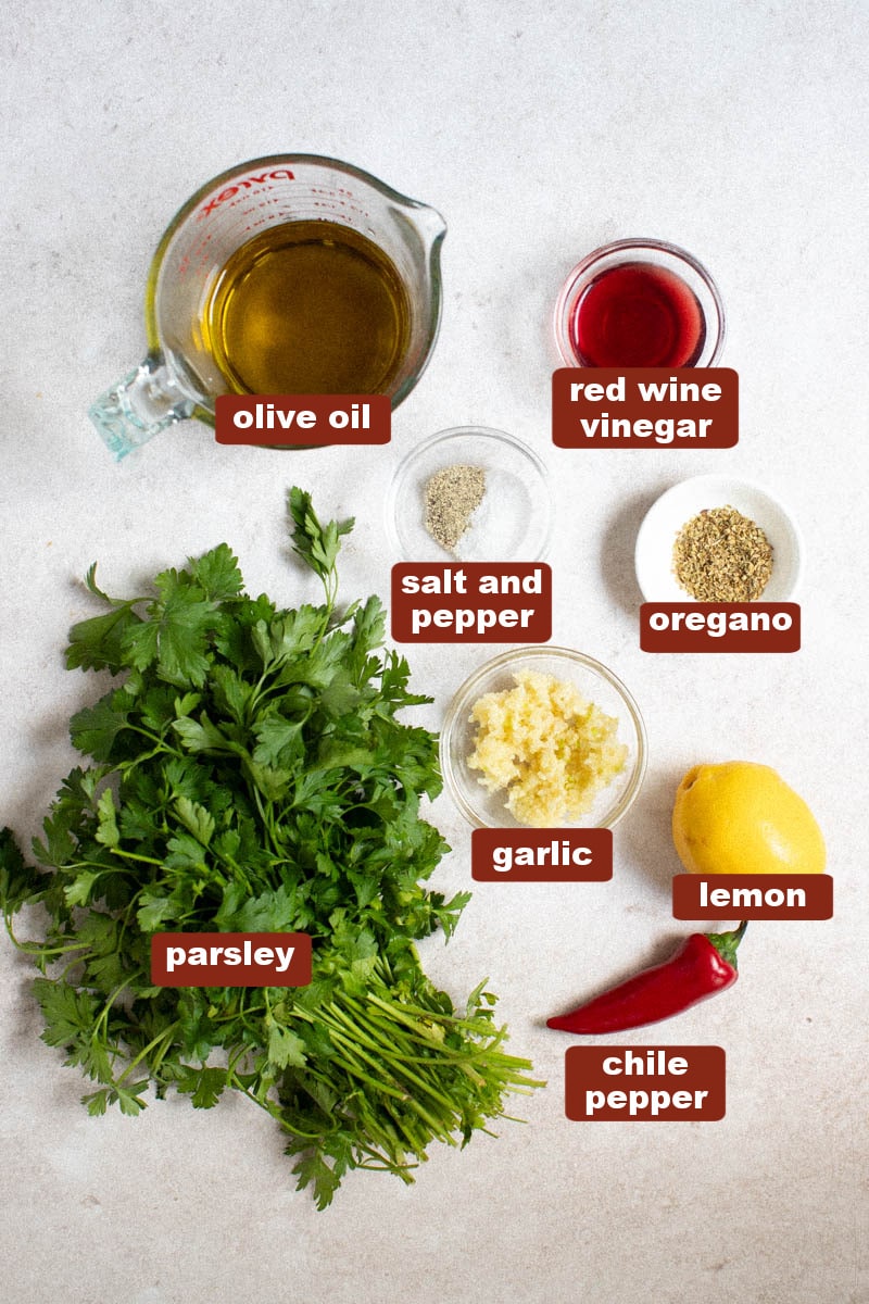 All of the ingredients for chimichurri sauce in small bowls on a white countertop.