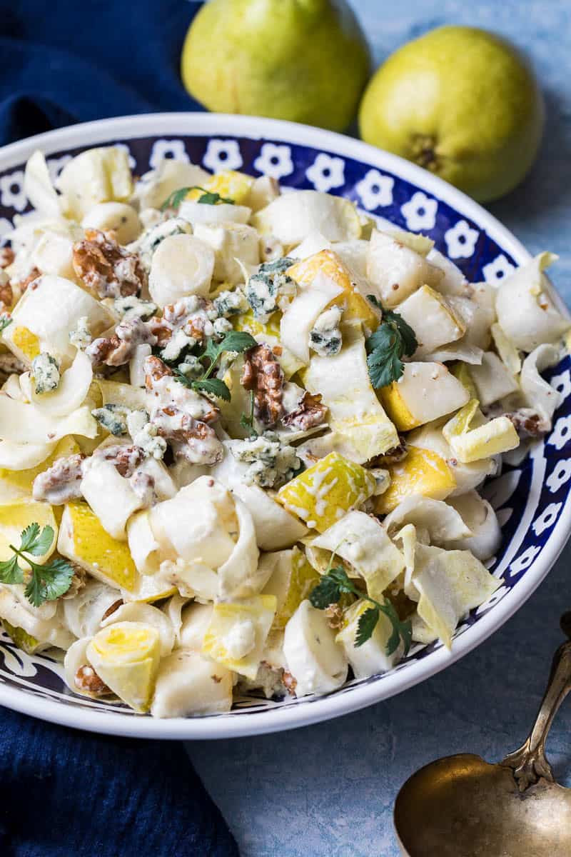 A bowl of salad with chopped endive, pear, walnuts, blue cheese, and a creamy dressing, garnished with parsley.