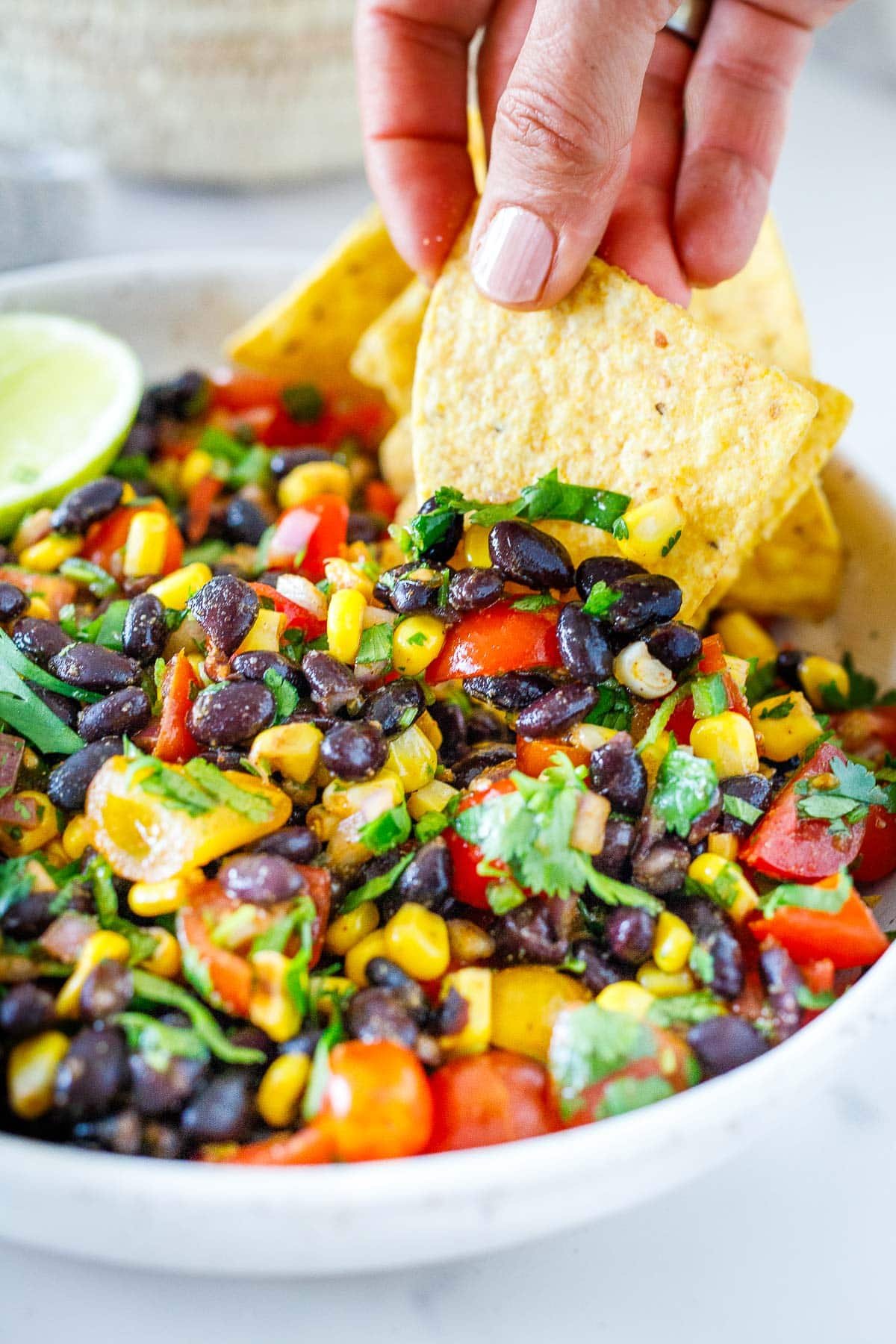 Dipping a chip into a bowl of black bean salsa with cherry tomatoes, corn, and cilantro.