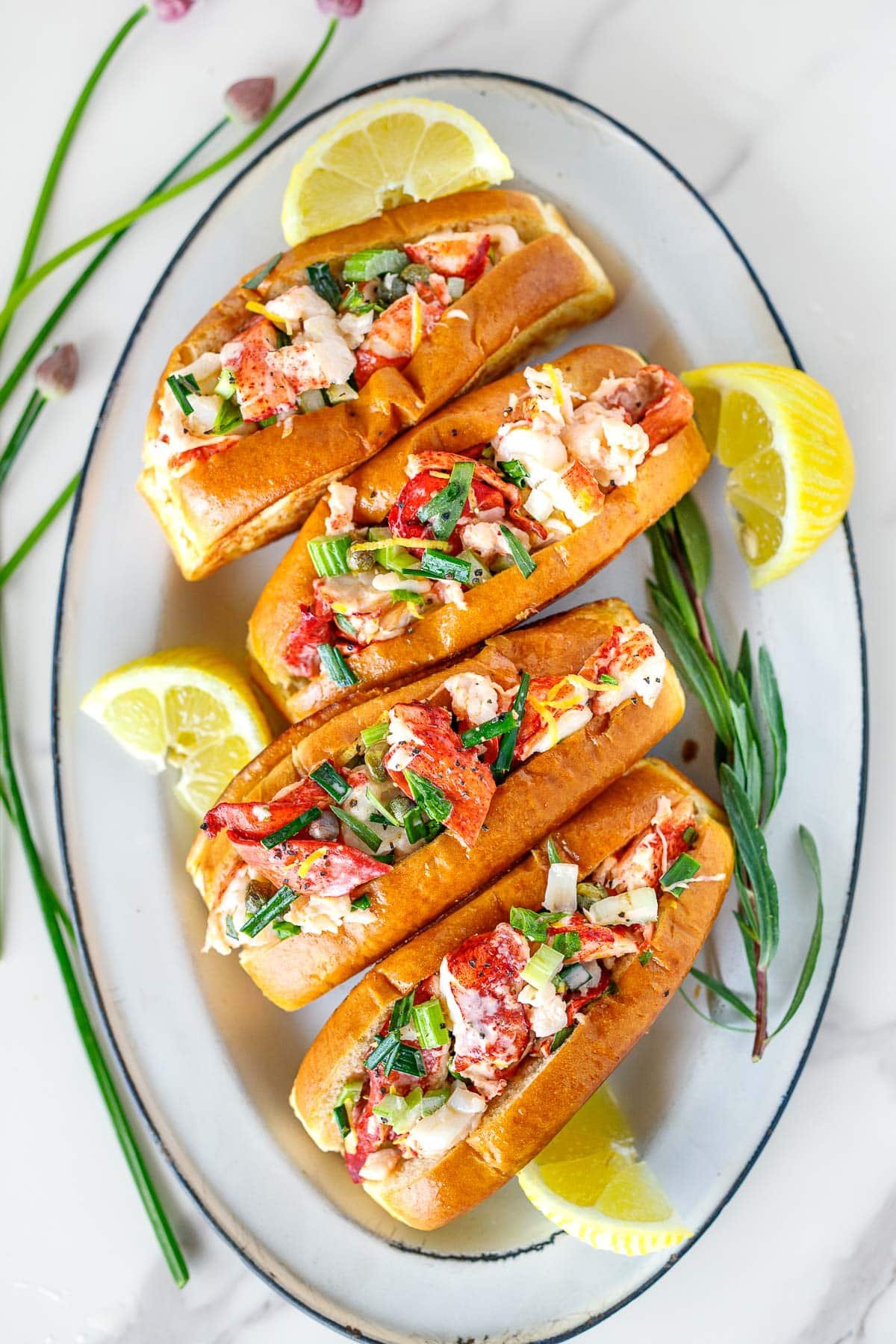 Lobster Rolls on an oval platter with herbs and lemon wedges.