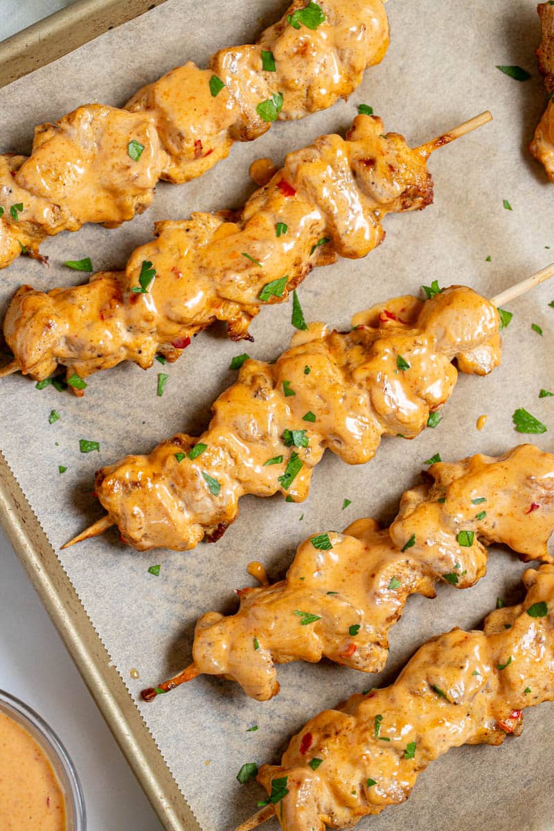 Five Bang Bang Chicken Skewers on a sheet pan after baking with a small amount of parsley as garnish.