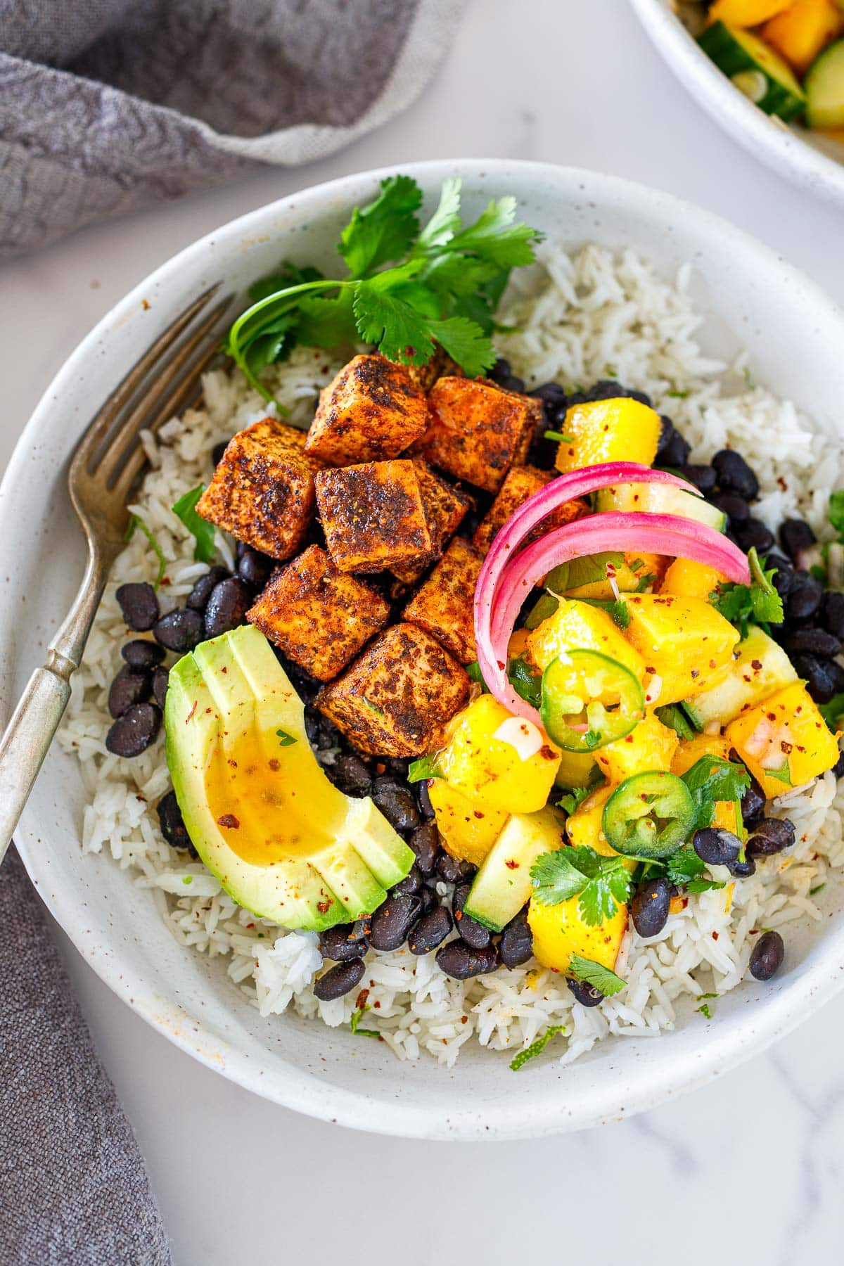 Spicy jerk tofu bowl garnished with mango salad, pickled onions, and avocado.