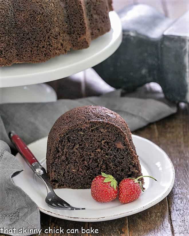 Slice of zucchini cake on a white plate with the whole cake in the background.