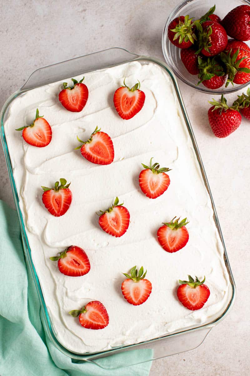 A whole strawberry tres leches cake on a countertop, ready to be served.