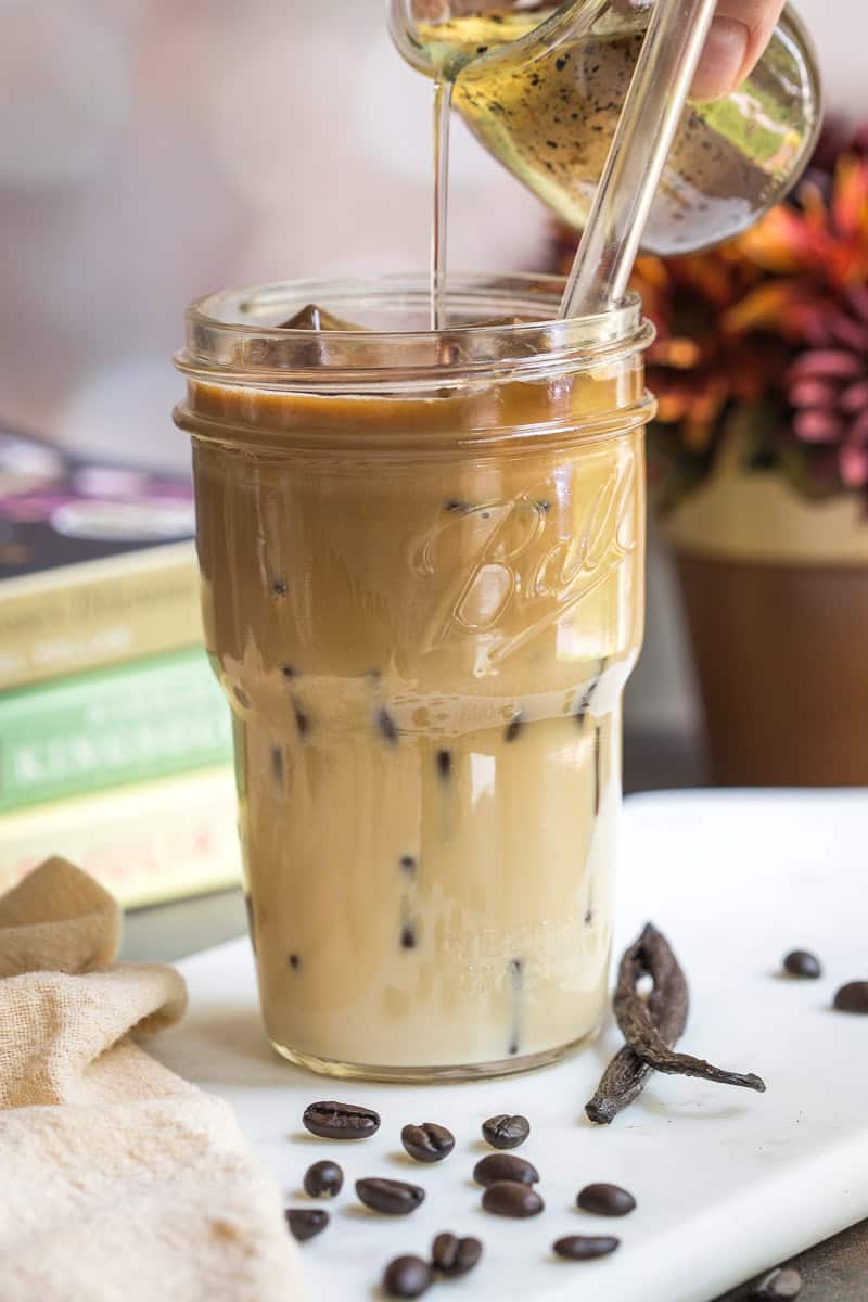Pouring vanilla syrup into an iced coffee in a mason jar.