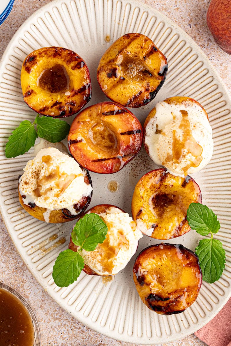 Grilled peaches with ice cream and mint leaves on a white serving plate.