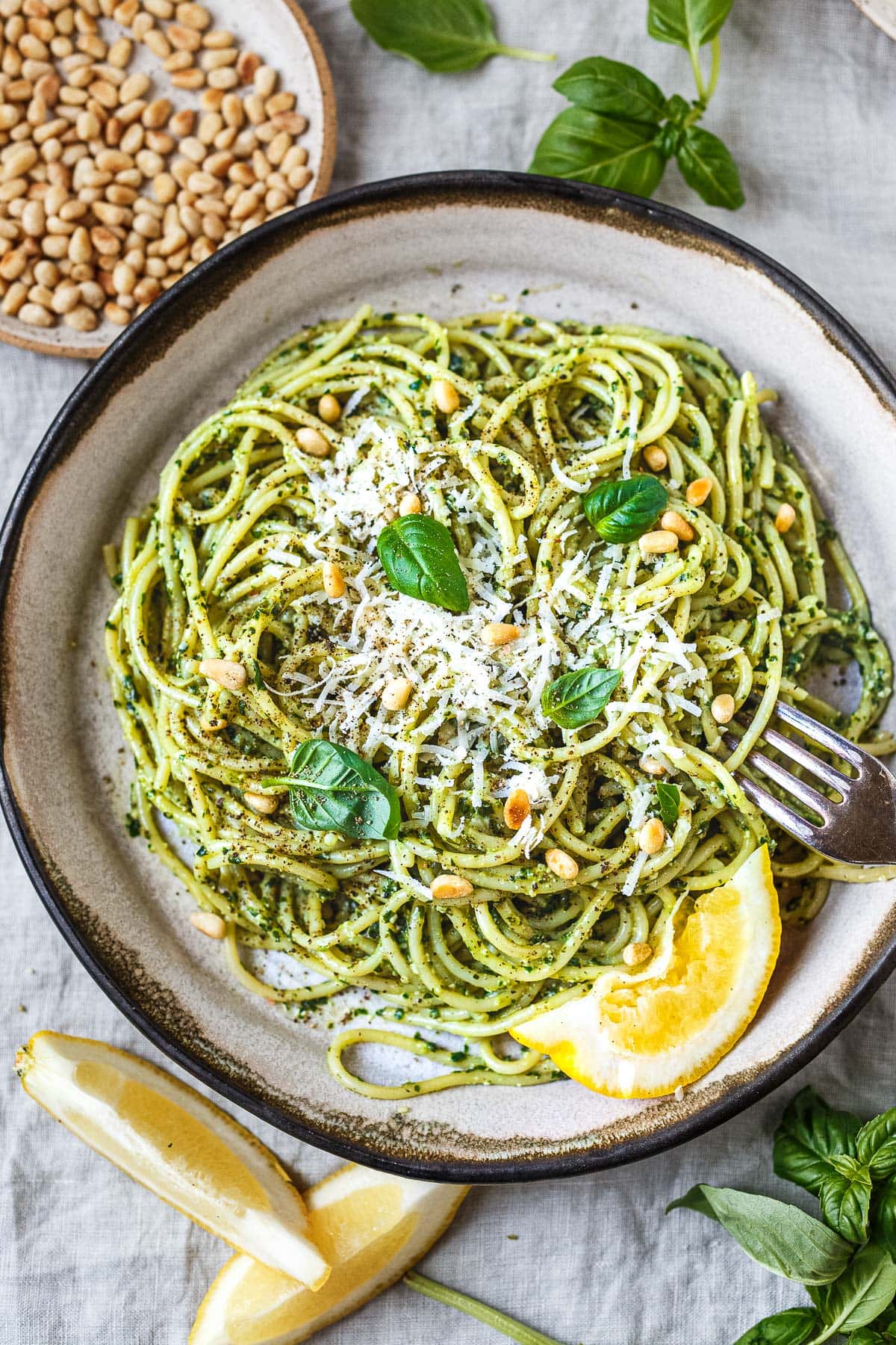 Bowl of pesto pasta topped with pine nuts, parmesan, fresh basil, and lemon