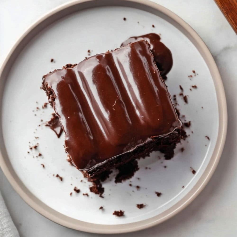 A slice of bumpy cake on a plate, topped with glossy chocolate fudge icing.
