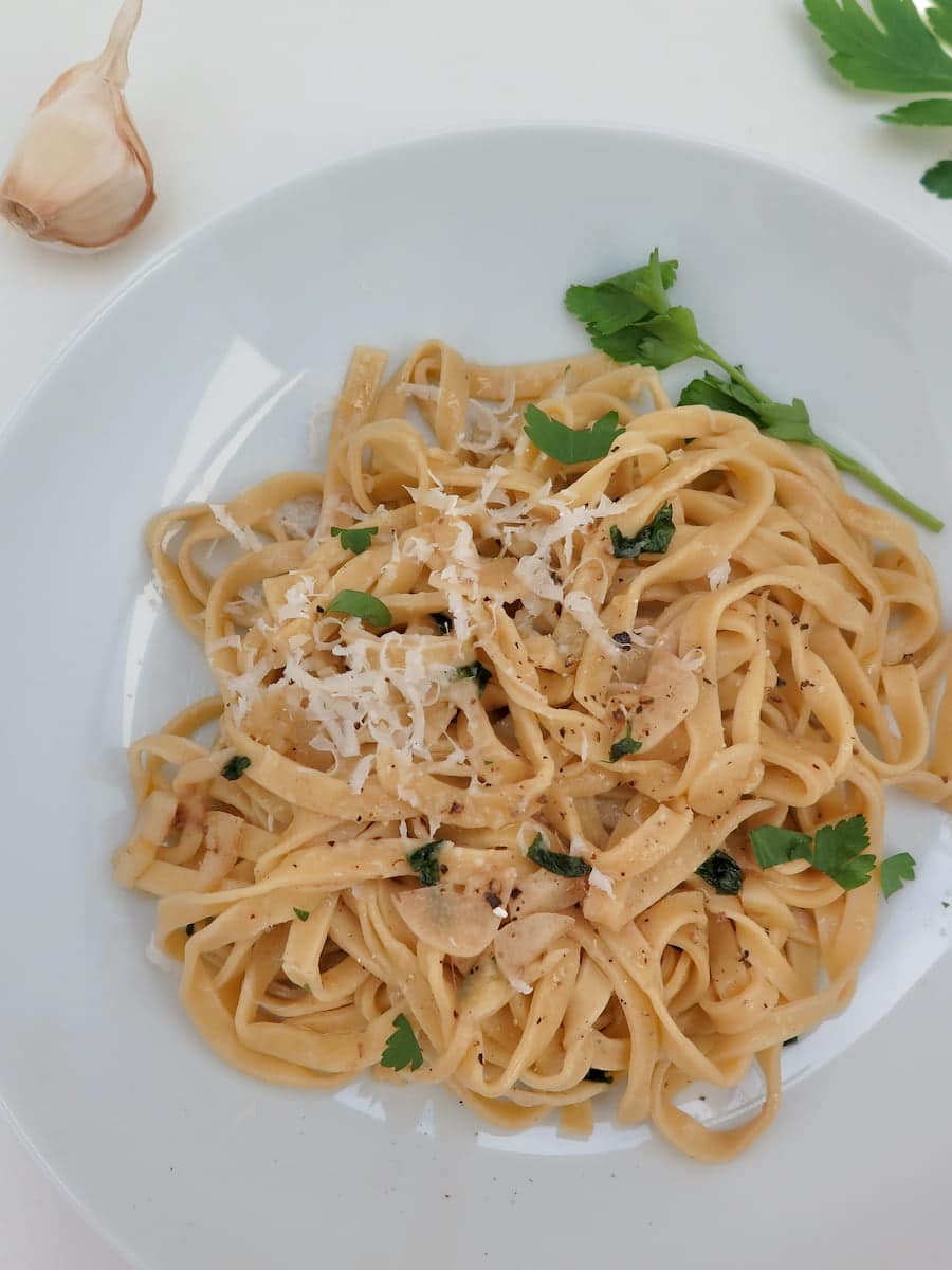 Bowl of flat egg noodles topped with grated cheese and parsley