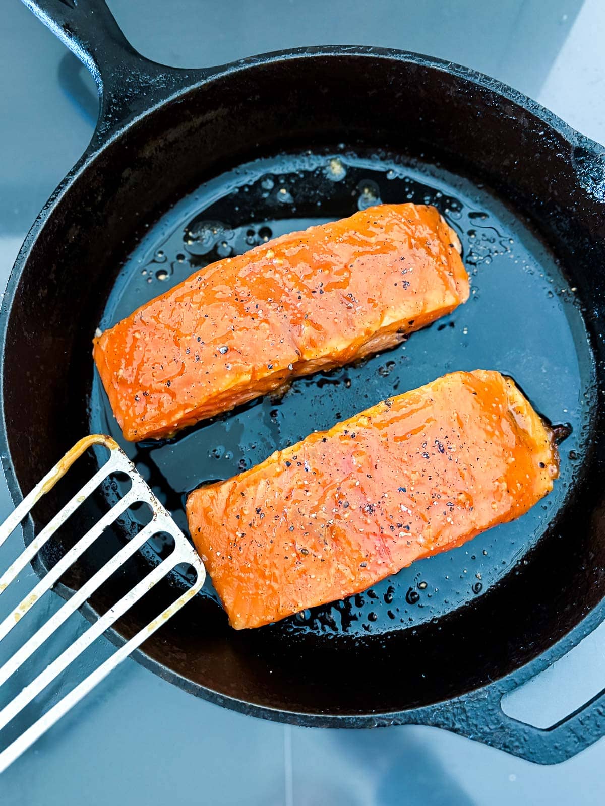 Two salmon filets searing in a skillet.