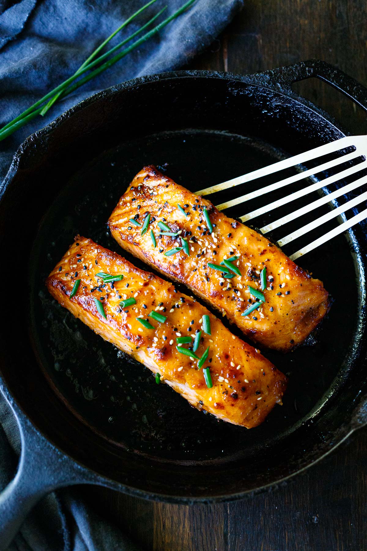 Two broiled salmon filets in a skillet with sesame seeds and chives.