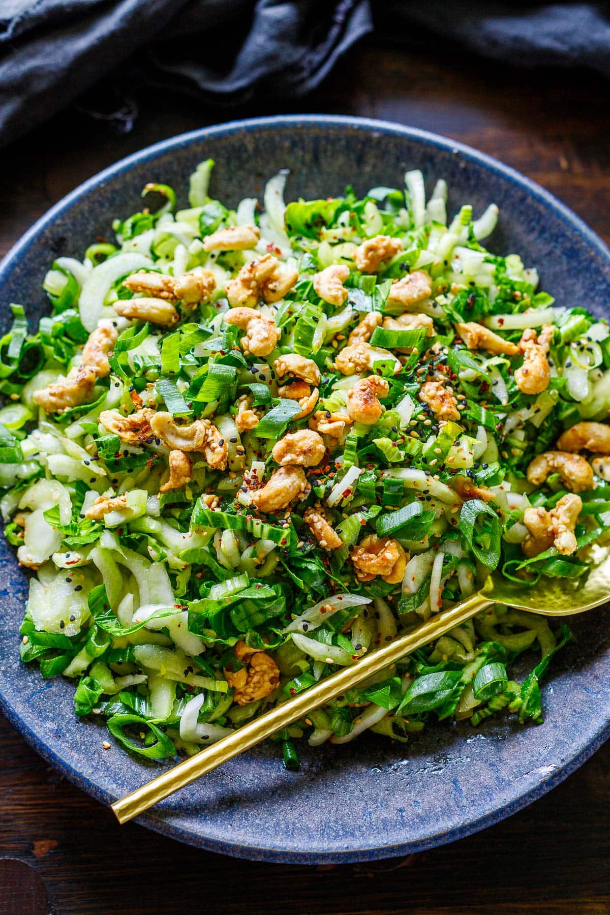 A bowl of bok choy salad filled with vibrant ingredients and topped with cashew brittle and sesame ginger dressing.