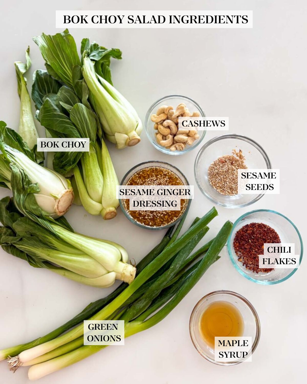 Ingredients for bok choy salad neatly arranged - bok choy heads, green onions, cashews, sesame ginger dressing, sesame seeds, chili flakes, and maple syrup.