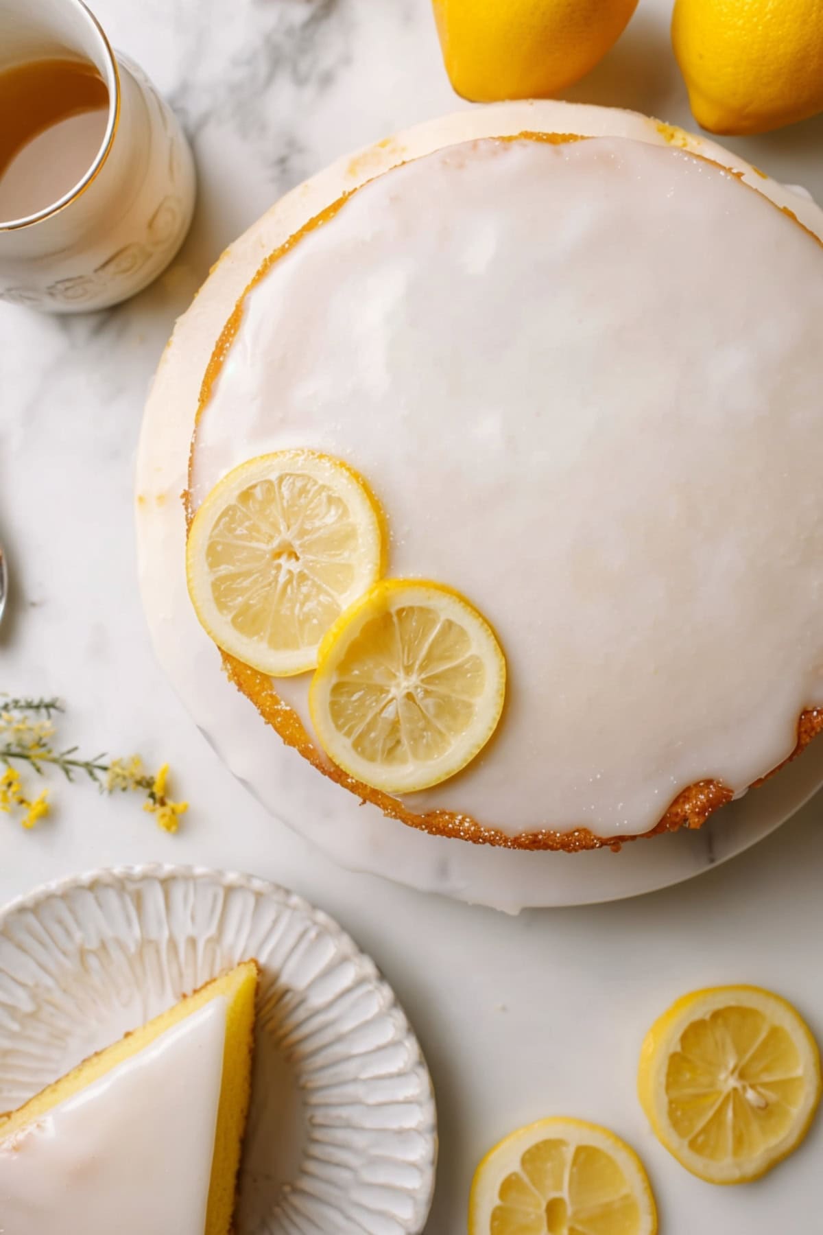 Glazed lemon olive oil cake, surrounded by fresh lemons and a slice served on a plate.