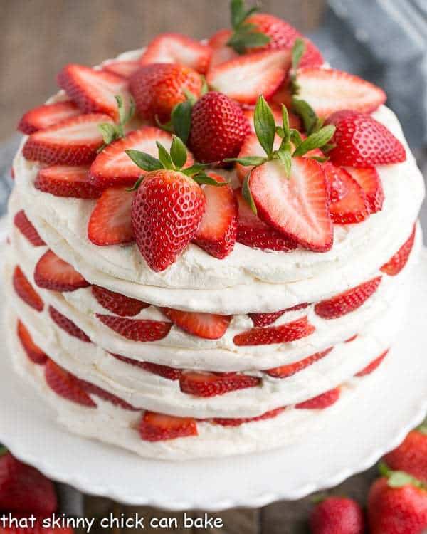 Fresh Strawberry Meringue Cake on a white cake plate garnished with sliced fresh strawberries.