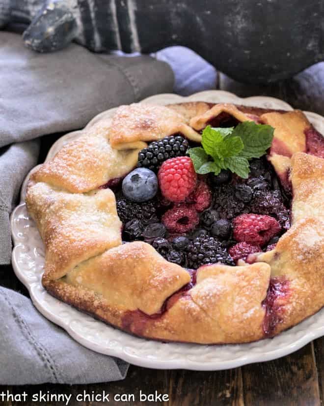 Mixed berry galette with a sprig of mint on a decorative white serving plate.