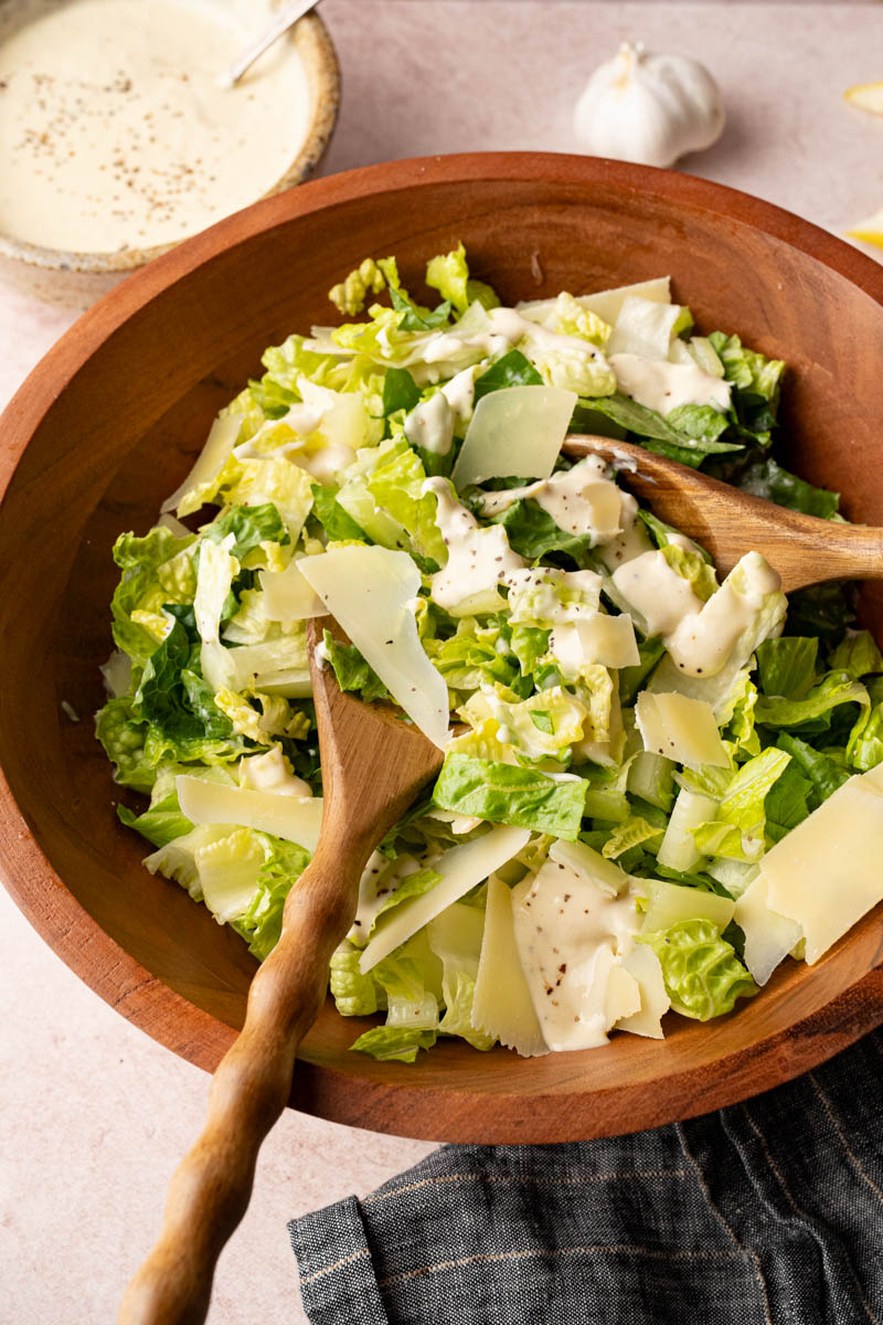 Tossing together the romaine lettuce, Parmesan cheese, and homemade Caesar dressing in a wooden bowl before serving.