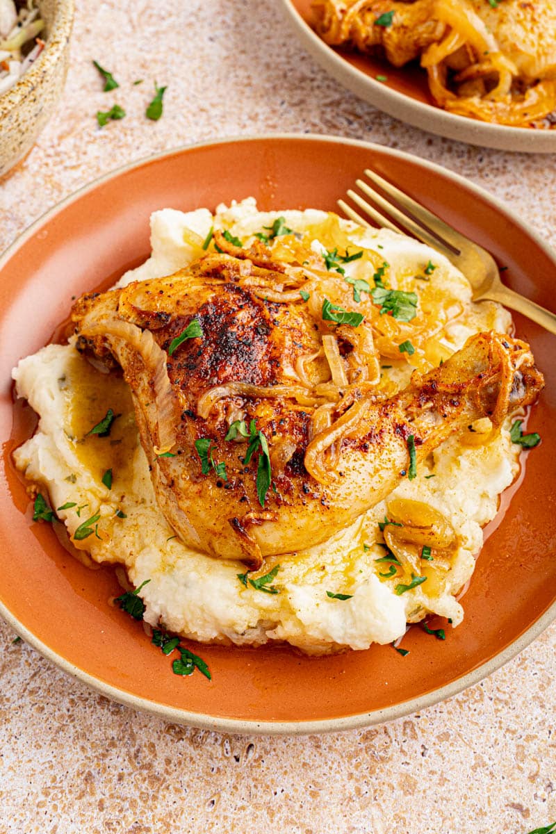 A roasted chicken quarter on a pile of mashed potatoes for serving.
