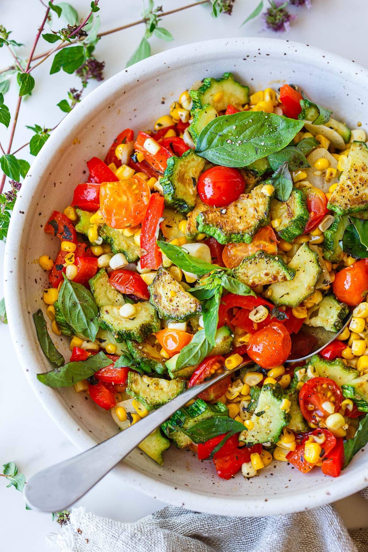Bowl of sautéed zucchini with corn, cherry tomatoes, bell peppers, and basil.