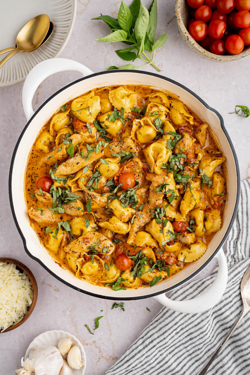 Creamy chicken tortellini in a pan before serving, garnished with fresh basil.