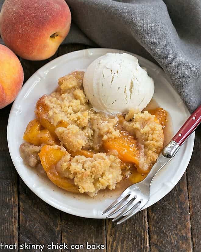 Overhead view of a Classic Peach Crisp on a white plate with a scoop of vanilla ice cream.