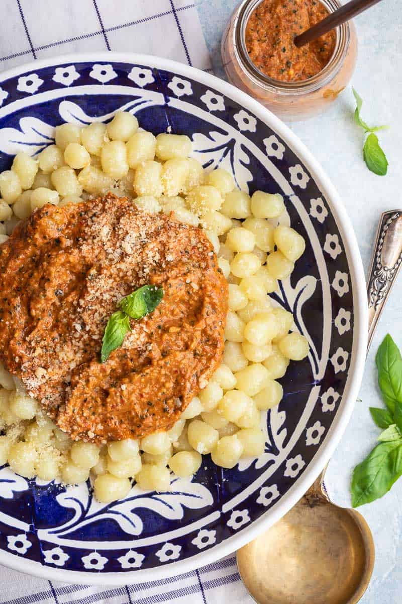 A plate of gnocchi topped with red pesto sauce and garnished with grated cheese and a basil leaf.