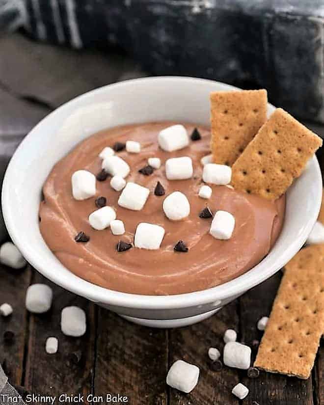 Easy S'mores Dessert Dip in a white bowl topped with mini marshmallows and chocolate chips, served with graham crackers.