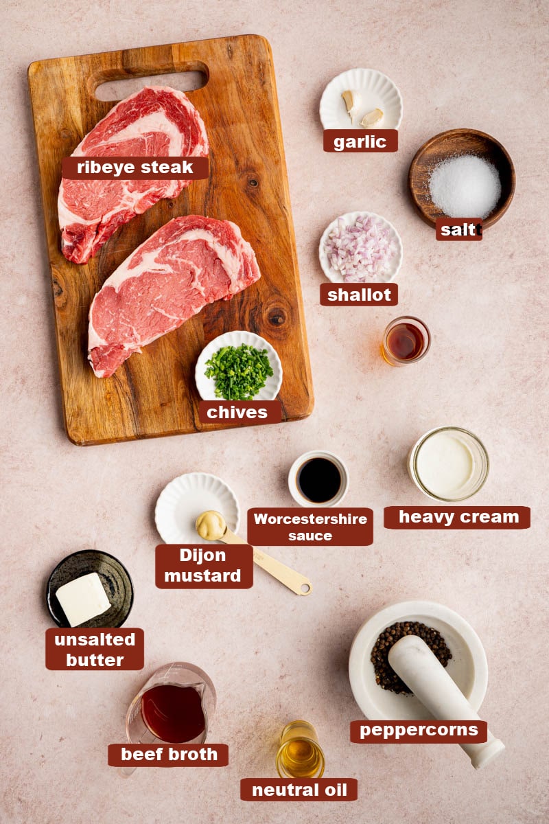 All of the ingredients for steak au poivre in bowls on a kitchen counter and the steak on a wooden cutting board.