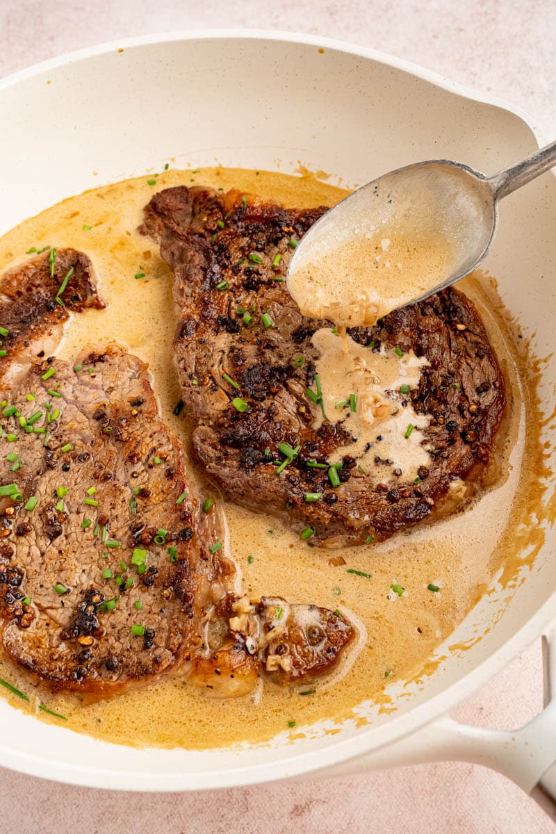 A spoon drips cognac sauce over the steak nestled in the pan.